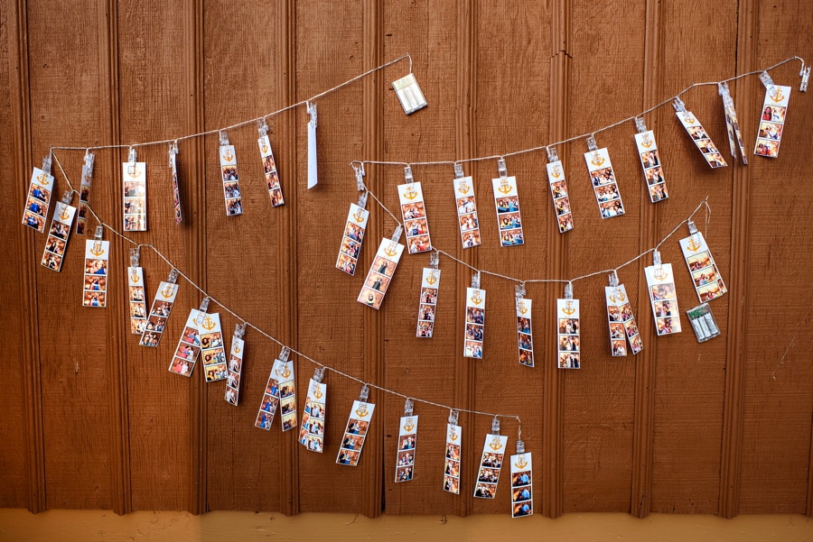 Photo booth strips hung on a wire on a brown barn at a wedding.